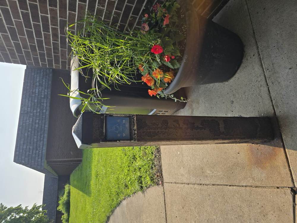 Corroded accessible door-opener post at the main entrance, with the wheelchair symbol plate weathered